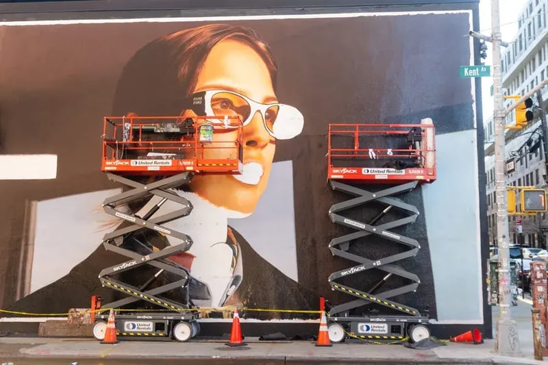 Workers on scissor lifts painting a large billboard