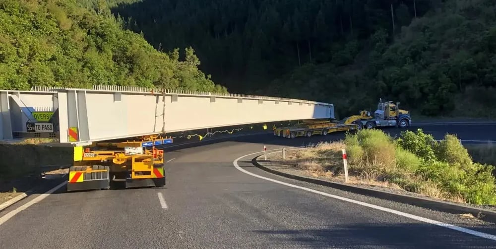 Heavy haulage truck carrying a long bridge beam along a winding road
