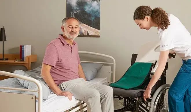 Novis team member preparing a wheelchair beside a client sitting on a hospital bed