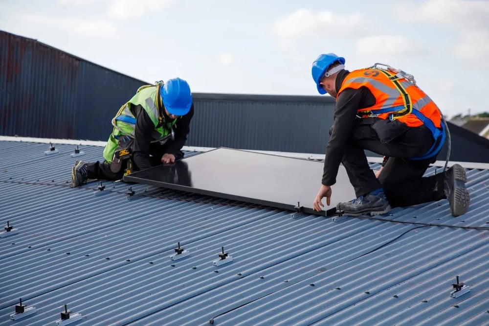 Two installers fitting a solar panel on a corrugated iron roof